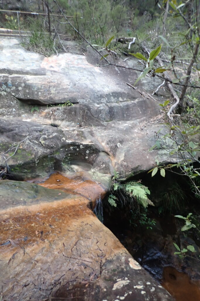 Water running over sandstone ledge into rock pool.